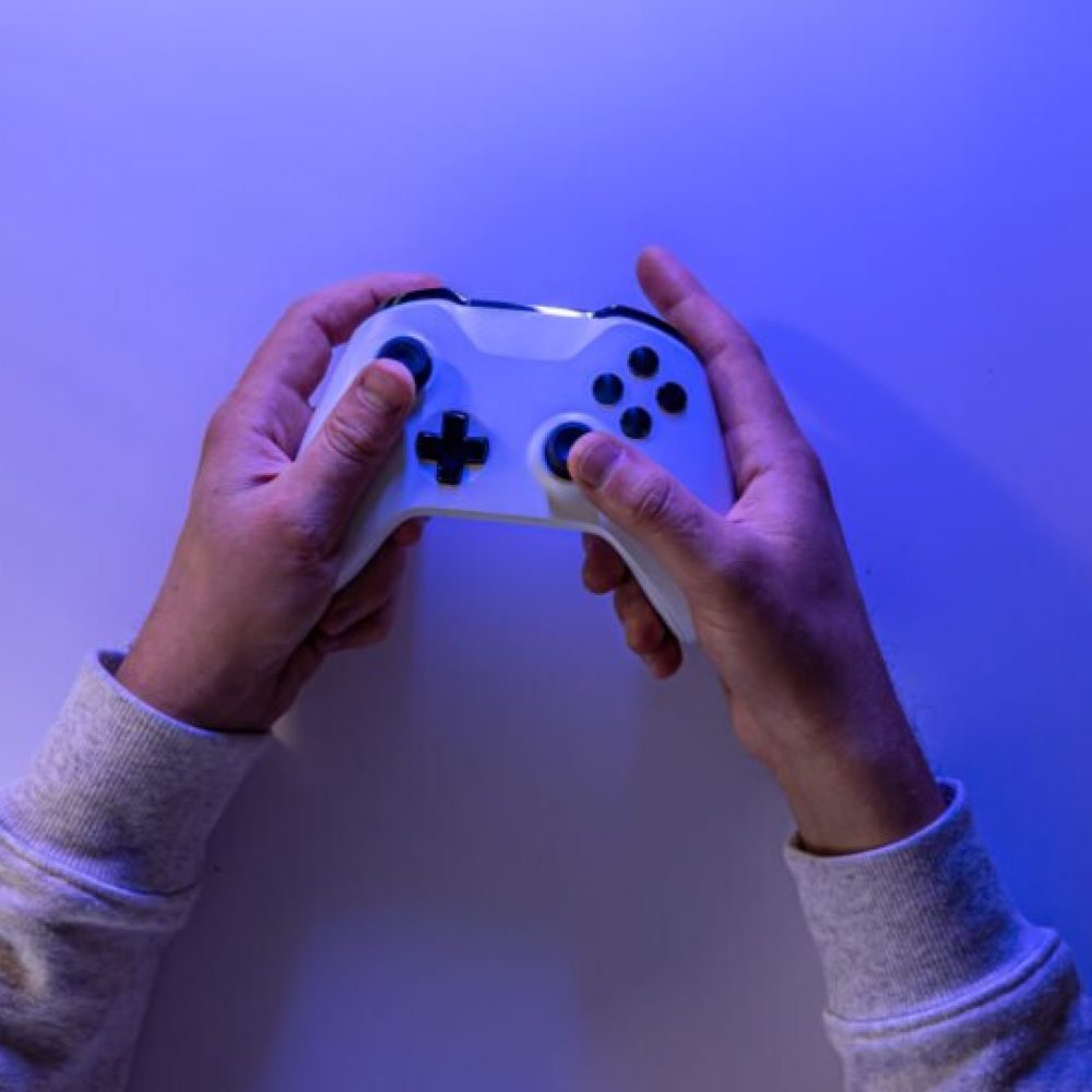 Male hands hold a gamepad on a blue background. Concept of the game, e-sports, leisure, gaming industry, video games. Banner. Flat lay, top view.